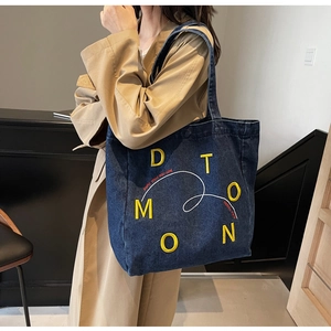 Detail of blue denim tote bag featuring yellow D T O M O N lettering and sturdy shoulder strap