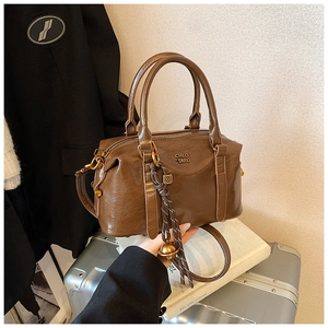 Detail of dark brown glossy PU leather handbag featuring metal logo and decorative charm