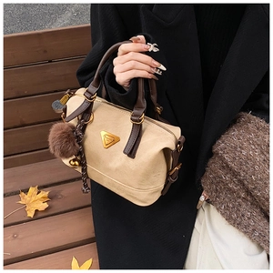 Close-up of beige Boston bag with brown handles and a plush pompom charm on a wooden bench