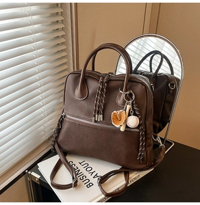 Dettaglio della borsa in pelle marrone scuro con tasca a zip e ciondolo da baseball