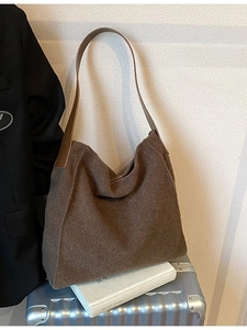 Bolso tote de lana marrón con correas de cuero sobre una maleta en un entorno de moda