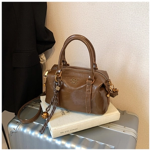 Detail of a brown polished leather bowling bag featuring golden text and a woven charm