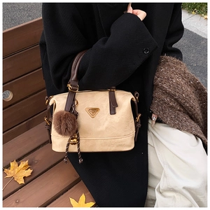 Detail of beige suede Boston bag featuring brown handles and a gold triangular plaque