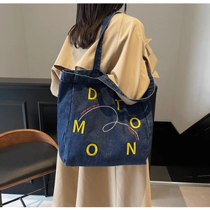 Detail of blue denim tote bag with embroidered letters and slogan for daily casual use