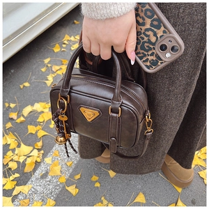Detail der braunen Ledertasche mit goldenem Logo und geflochtenem Glockenanhänger