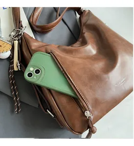 Detail view of brown leather tote bag with front zipper pocket and baseball charm