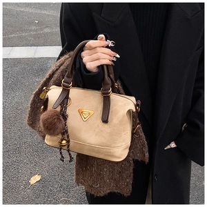 Detail of khaki suede pillow bag featuring a signature metal logo and brown leather handles