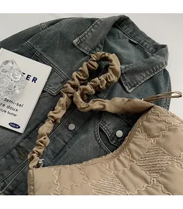 Detail of beige quilted tote bag with pleated strap on denim jacket and magazine