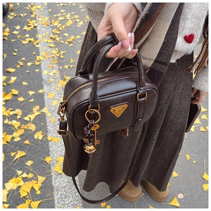 Nahaufnahme der braunen Vintage-Handtasche mit Metalldreieck-Logo und goldenem Schlüsselanhänger
