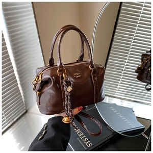 Close-up of vintage dark brown Boston bag with polished leather finish and woven charm