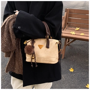 Detail of beige frosted handbag featuring dark brown leather handles and gold metal logo