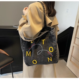 Detailed shot of oversized washed denim tote bag with vibrant yellow embroidery letters