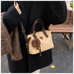 Detail of minimalist beige suede bag with brown leather handles and gold triangle logo