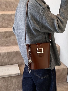 Sac seau marron vintage avec boucle argentée et pompon porté par un mannequin