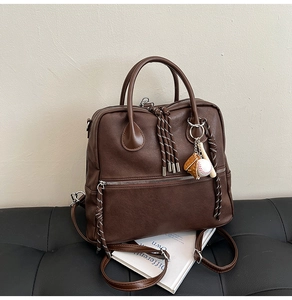 Dettaglio cartella vintage marrone con ciondolo da baseball su panca nera