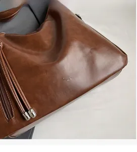 Detail of brown leather tote bag showing fine texture, metal zipper and brand logo