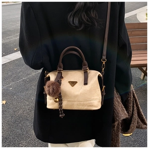 Chic beige crossbody pillow bag with brown handles and pompom on autumn street view