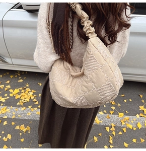 Detail of beige quilted nylon tote bag with pleated ruched strap and wavy embroidery