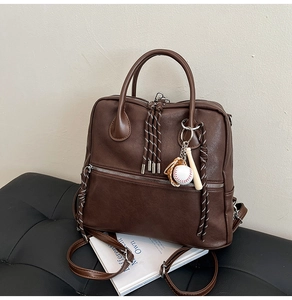 Dettaglio borsa vintage in pelle marrone con ciondoli da baseball e cordini intrecciati