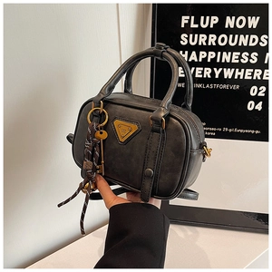 Detail der grauen Retro-Boston-Tasche mit goldenem Dreieckslogo und Zieranhänger