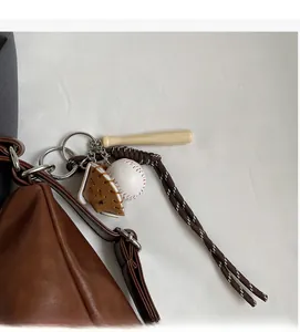 Detail of baseball keychain with mini bat and glove hanging on a brown leather tote bag