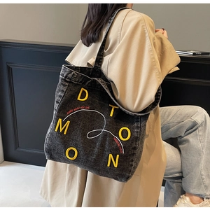 Close-up of black denim tote bag with yellow letters and freedom slogan embroidery