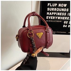 Detail einer dunkelroten Vintage-Lederhandtasche mit Goldemblem und Anhänger
