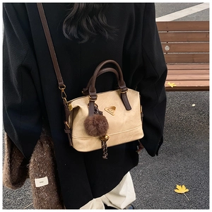 Detail view of a beige minimalist pillow bag with dark brown handles and plush charm