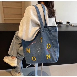 Detail of large denim tote bag featuring yellow letter embroidery and sturdy shoulder straps