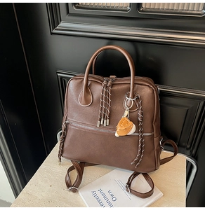 Dettaglio borsa in similpelle marrone con tirazip intrecciato e ciondolo da baseball