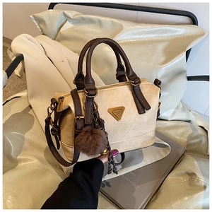Detailed close-up of beige suede Boston bag featuring brown trim and a plush ball charm