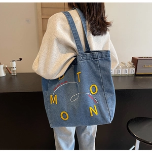 Detail of blue denim tote bag featuring yellow Moon embroidery and white scroll patterns