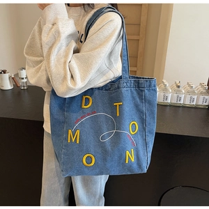 Detail of blue denim tote bag with 3D yellow D T M O O N embroidery and casual shoulder strap