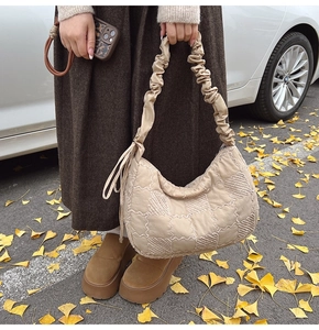 Detail view of quilted beige nylon tote bag with ruffled handle and tassel on autumn street