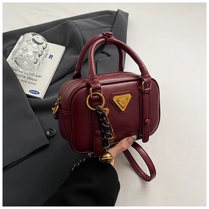 Detail der weinroten Lederhandtasche mit goldenem Dreieckslogo und geflochtenem Anhänger
