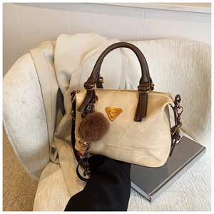 Detail view of beige Boston bag with brown faux fur pom pom on a stylish chair