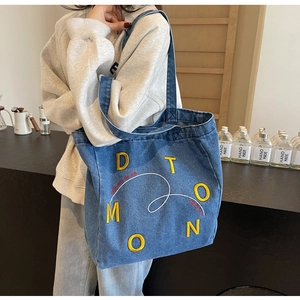 Detail of blue denim tote bag with yellow embroidery and wide shoulder strap