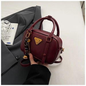 Detailansicht der weinroten Vintage-Handtasche mit goldenem Logo und elegantem Anhänger