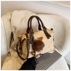 Detail of a beige pillow bag featuring brown leather straps and a fuzzy ball charm
