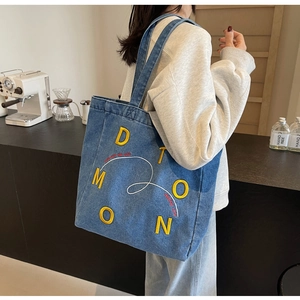 Detail shot of blue denim tote bag featuring yellow letter embroidery and sturdy handles