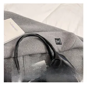Detail of glossy black leather tote handle with long ribbon accent on a grey coat