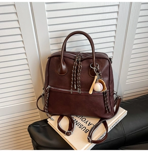Dettaglio zaino in pelle bordeaux con ciondolo da baseball e tiranti intrecciati