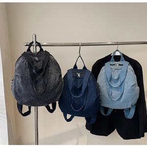 Detailed view of large denim backpacks in black, dark blue, and light blue on a metal rack