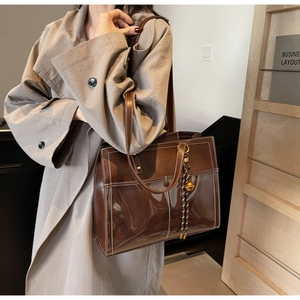 Detail of dark brown tote bag with white contrast stitching and gold ball charm accessory