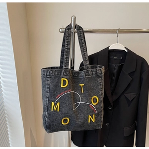 Detail of dark grey denim tote bag with bright yellow embroidery and slogan text