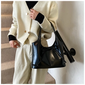 Detail of glossy black shoulder bag with decorative bow and premium synthetic leather finish