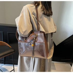 Close-up of brown leather and PVC tote bag with bell pendant on shoulder