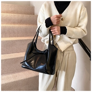 Detailed view of a black matte leather tote bag featuring an elegant bow tie decoration