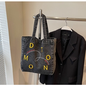 Detail of black denim tote bag with yellow DIOMON embroidery and red slogan text