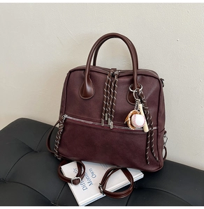 Dettaglio dello zaino in pelle bordeaux con tiranti a righe e ciondolo da baseball sportivo